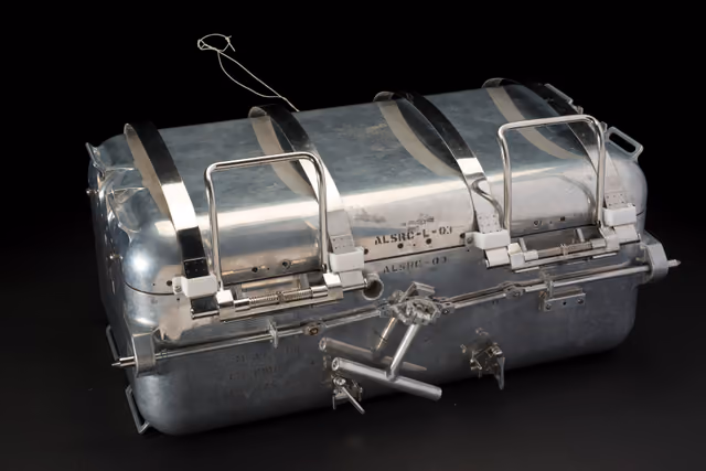 The Apollo 11 Lunar Sample Return Container, an aluminium box with heavy latches and a sealing rim, photographed in museum lighting.