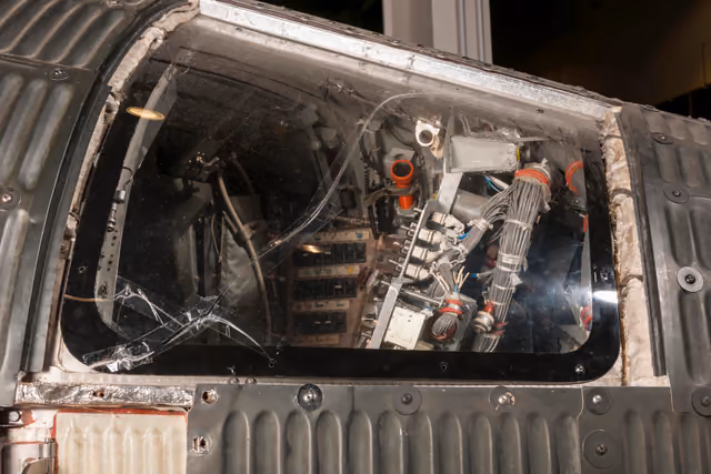 The Mercury capsule flown on MA-6, a small bell-shaped spacecraft with a scorched heat shield and a narrow hatch, photographed in museum lighting.
