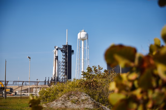 A Falcon 9 rocket with a Dragon spacecraft standing vertical at Launch Complex 39A, the pad structure and lightning towers around it.