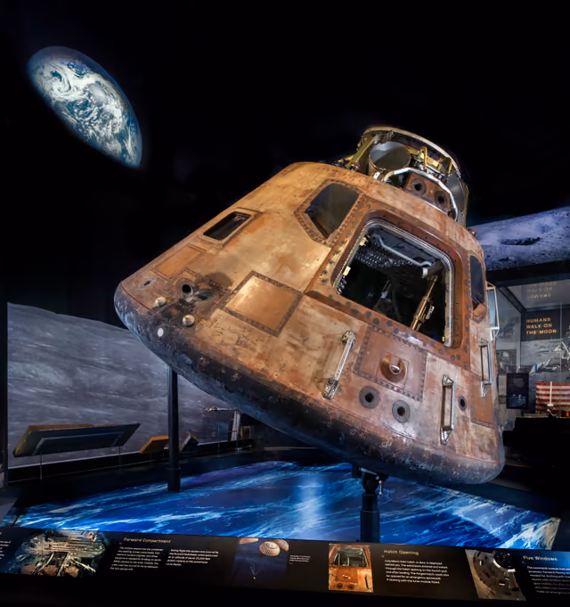 The Apollo 11 command module, a scorched conical spacecraft, photographed in a museum gallery.